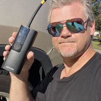 A man in a cap and glasses holds up a black box containing a jet blower kit.